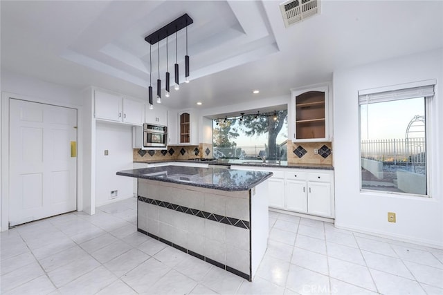 kitchen featuring a center island, hanging light fixtures, a raised ceiling, dark stone counters, and white cabinets