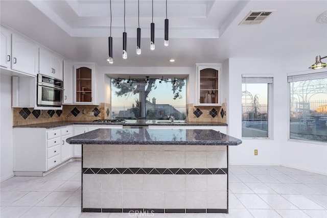 kitchen with a raised ceiling, hanging light fixtures, a center island, and dark stone counters