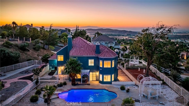 back house at dusk featuring a fenced in pool, a mountain view, and a patio