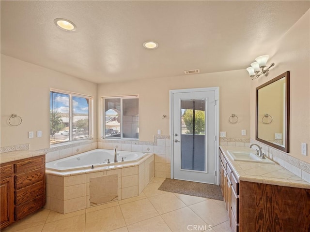 bathroom with a relaxing tiled tub, vanity, and tile patterned flooring