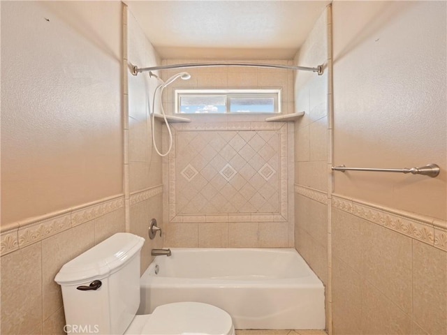 bathroom with toilet, tile walls, and tiled shower / bath