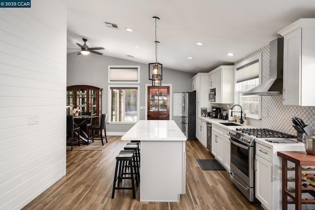 kitchen featuring stainless steel appliances, a center island, wall chimney exhaust hood, decorative light fixtures, and lofted ceiling