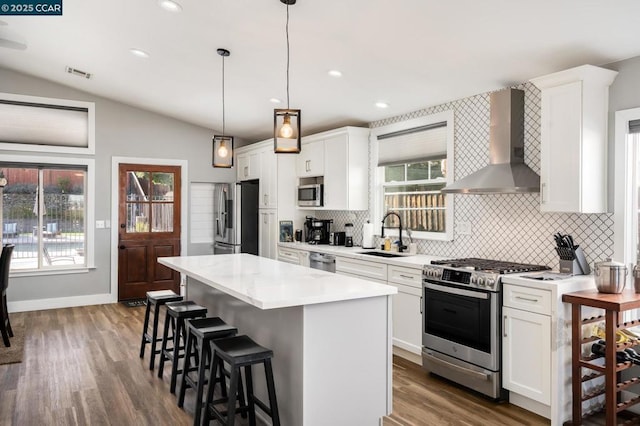 kitchen featuring vaulted ceiling, wall chimney exhaust hood, white cabinets, appliances with stainless steel finishes, and sink