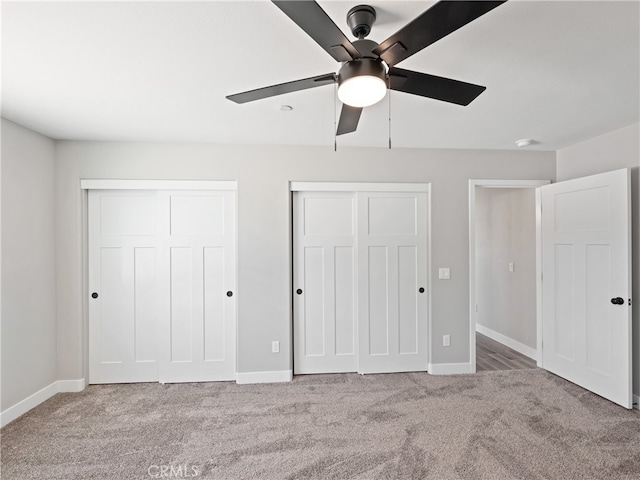 unfurnished bedroom with ceiling fan, light colored carpet, and multiple closets