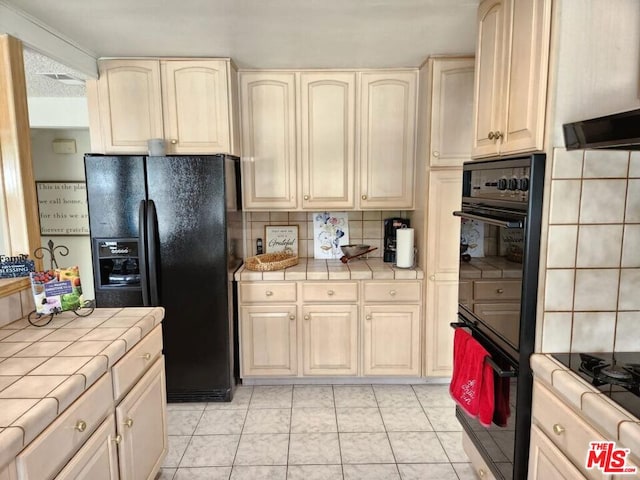 kitchen featuring black appliances, light tile patterned flooring, tile counters, and backsplash