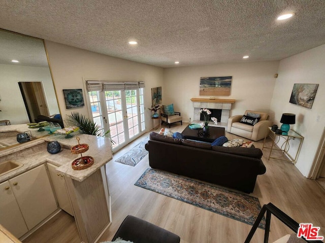 living room with french doors, a fireplace, a textured ceiling, and light hardwood / wood-style floors