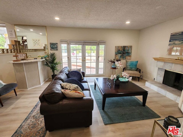 living room with a healthy amount of sunlight, a textured ceiling, light wood-type flooring, and a tile fireplace