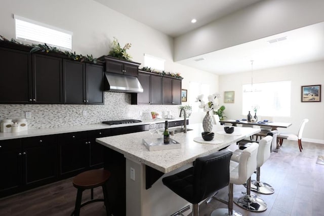 kitchen featuring hanging light fixtures, dark hardwood / wood-style flooring, a breakfast bar, and a kitchen island with sink