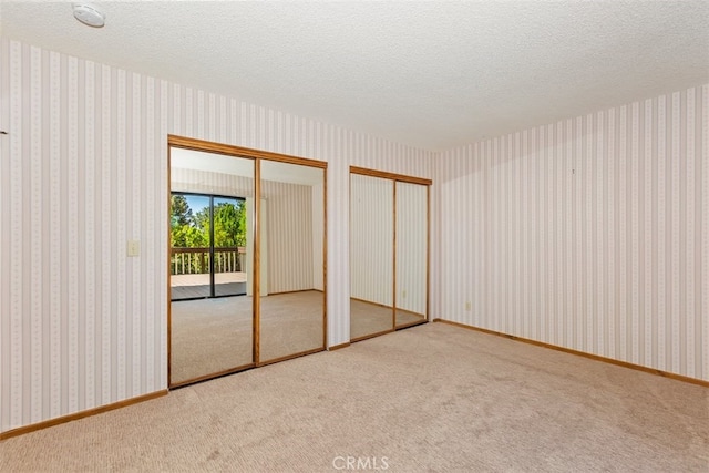 unfurnished bedroom featuring a textured ceiling, carpet, access to outside, and two closets