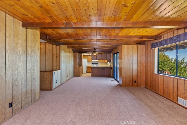 unfurnished living room featuring wood walls, light carpet, and beamed ceiling