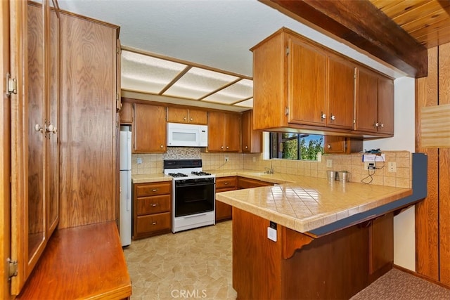 kitchen featuring a breakfast bar, backsplash, white appliances, kitchen peninsula, and sink