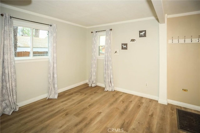 empty room featuring hardwood / wood-style floors, a wealth of natural light, ornamental molding, and beam ceiling