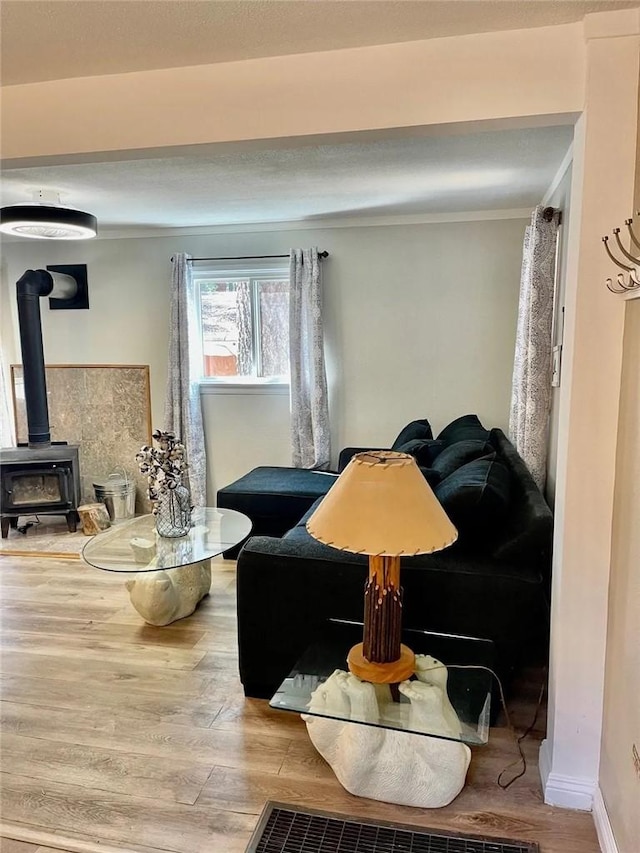 living area with ornamental molding, light wood-style flooring, a wood stove, and baseboards