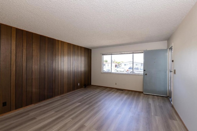 unfurnished room with wood-type flooring, wooden walls, and a textured ceiling