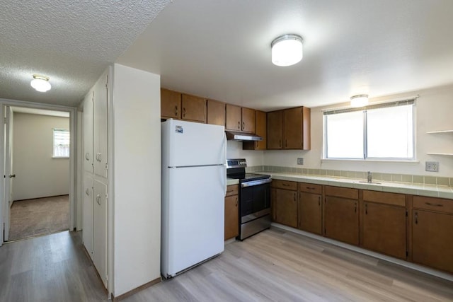 kitchen featuring sink, stainless steel range with electric stovetop, white refrigerator, tile counters, and a textured ceiling