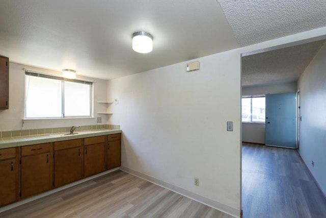 kitchen with tile counters, sink, and light hardwood / wood-style flooring