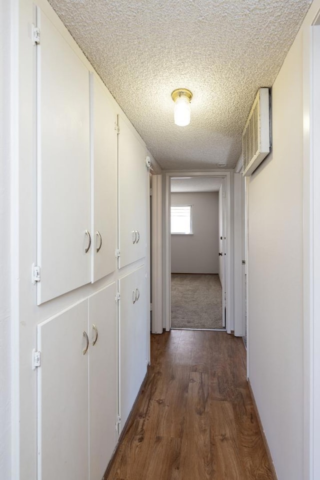 hall with dark wood-type flooring, a wall mounted AC, and a textured ceiling