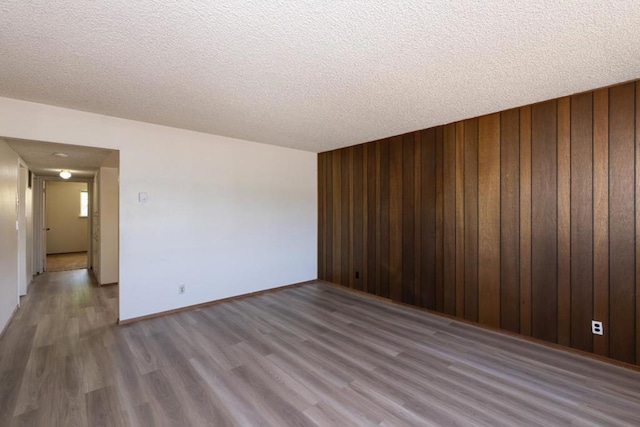 empty room with wood-type flooring, a textured ceiling, and wood walls