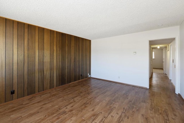 empty room with dark wood-type flooring, a textured ceiling, and wood walls