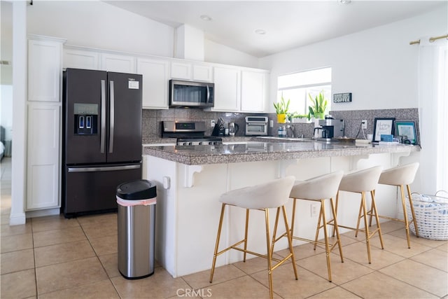 kitchen featuring stainless steel appliances, a breakfast bar, lofted ceiling, and white cabinetry