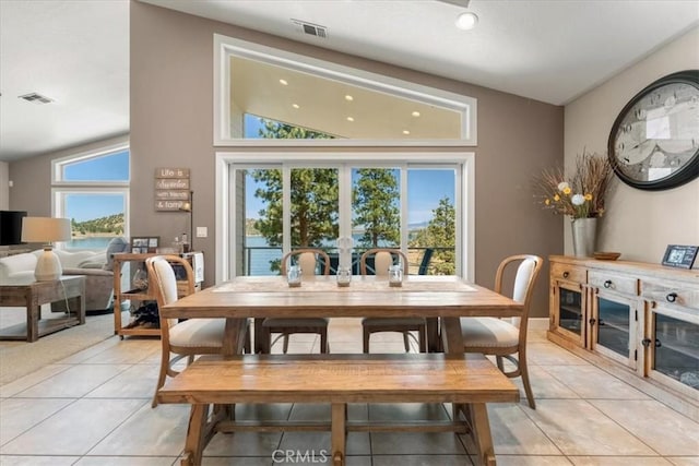 dining room featuring a water view, a wealth of natural light, light tile patterned flooring, and vaulted ceiling