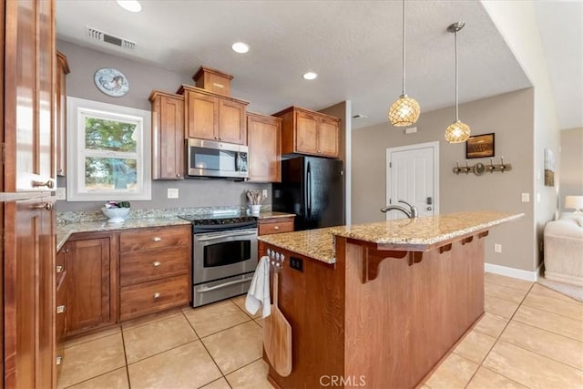 kitchen featuring light stone counters, stainless steel appliances, a kitchen island with sink, pendant lighting, and a breakfast bar area