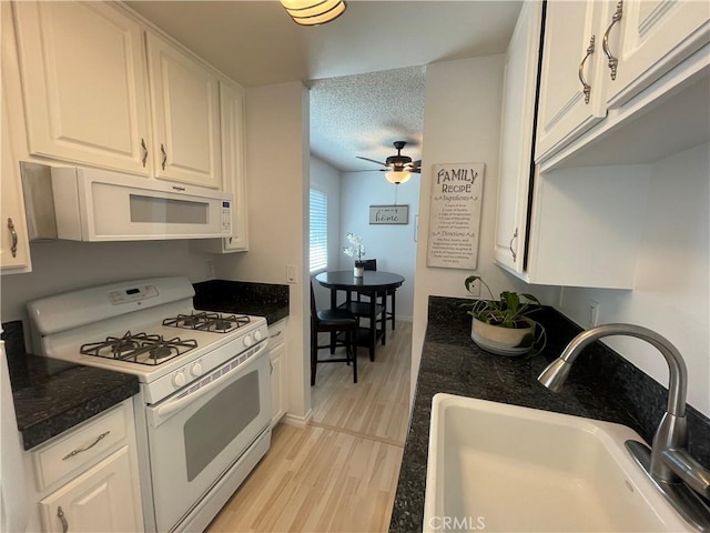 kitchen with a textured ceiling, white appliances, a sink, white cabinetry, and light wood-type flooring