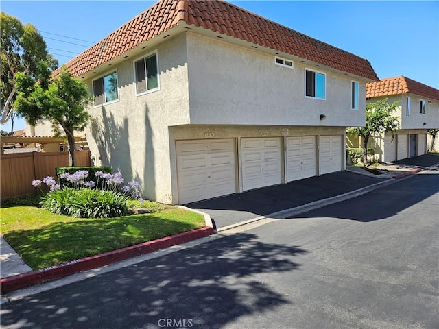 view of property exterior with community garages, a tiled roof, fence, and stucco siding