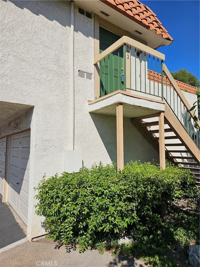 view of property exterior featuring a garage, a tiled roof, stairway, and stucco siding