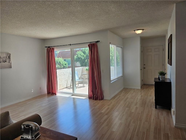 unfurnished living room with a textured ceiling, light wood-type flooring, and baseboards