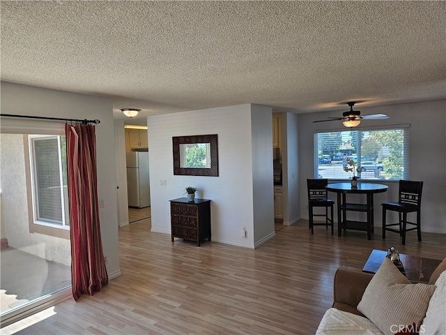 living area with a ceiling fan, a textured ceiling, baseboards, and wood finished floors