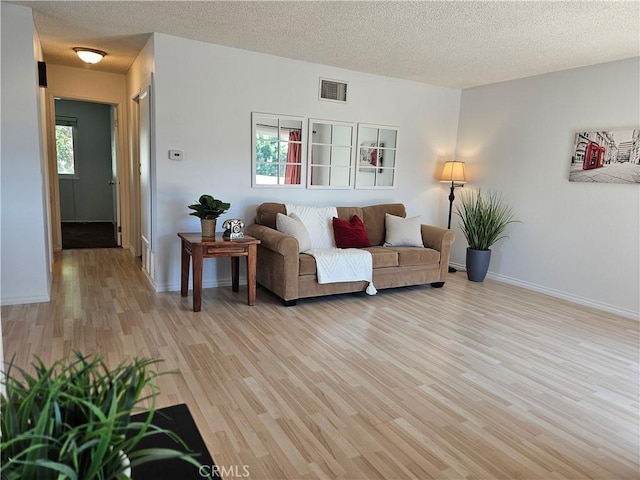 living area with light wood-type flooring, a healthy amount of sunlight, visible vents, and a textured ceiling