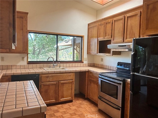 kitchen with black fridge, light parquet floors, tile counters, sink, and stainless steel electric range oven