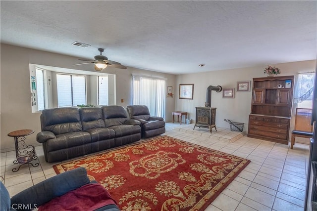 tiled living room with ceiling fan, a wood stove, and a textured ceiling