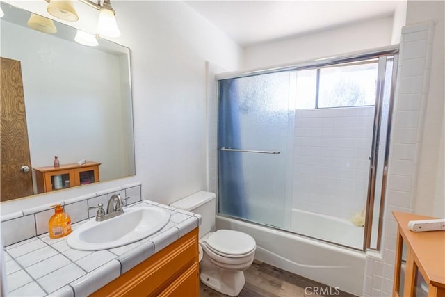 full bathroom with wood-type flooring, shower / bath combination with glass door, vanity, and toilet