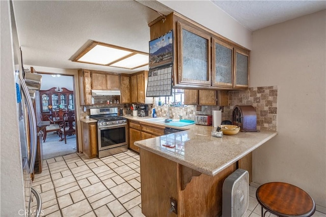 kitchen with appliances with stainless steel finishes, sink, backsplash, kitchen peninsula, and a breakfast bar area