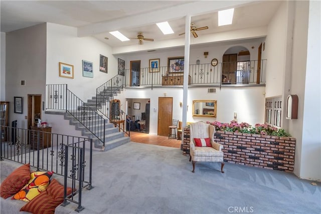 living room with ceiling fan, carpet, beamed ceiling, a skylight, and high vaulted ceiling