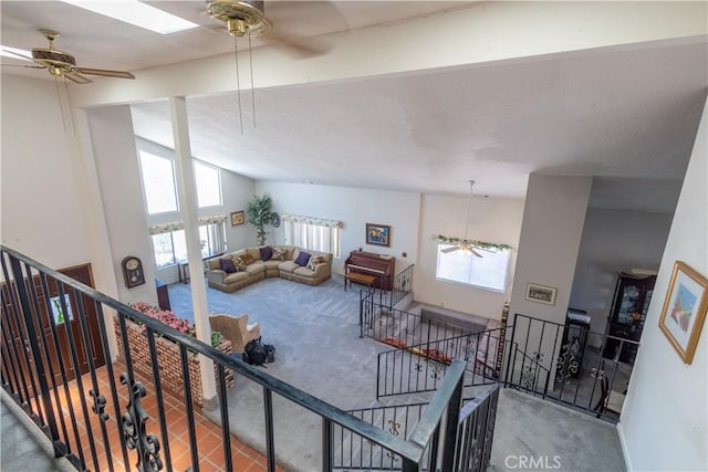 carpeted living room with ceiling fan and lofted ceiling with skylight