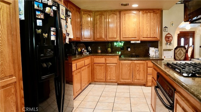 kitchen with backsplash, dark stone countertops, light tile patterned floors, and black appliances