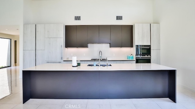 kitchen featuring gray cabinetry, a spacious island, sink, and multiple ovens