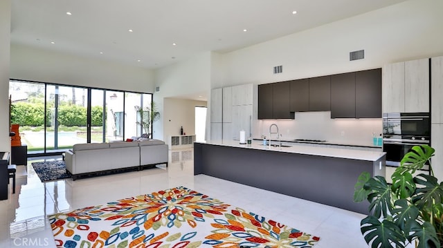 kitchen with backsplash, a towering ceiling, sink, and gas cooktop