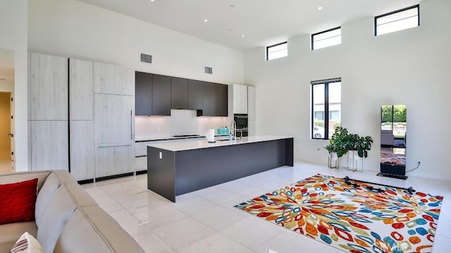 kitchen featuring a breakfast bar area, a kitchen island with sink, sink, and a towering ceiling