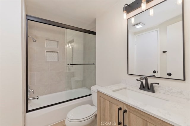 full bathroom with combined bath / shower with glass door, vanity, and toilet