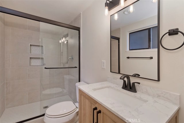 bathroom featuring a shower with shower door, vanity, and toilet