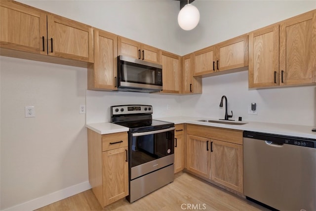 kitchen featuring pendant lighting, sink, stainless steel appliances, light brown cabinetry, and light hardwood / wood-style floors