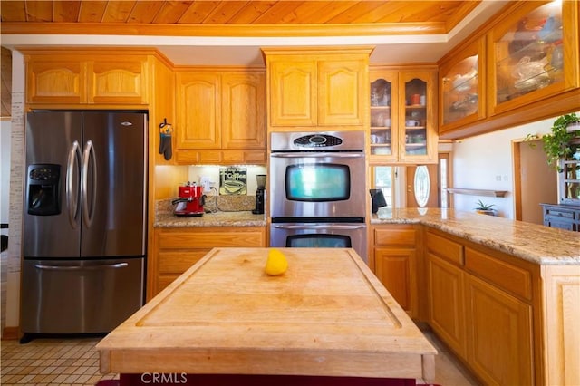 kitchen with a center island, wooden ceiling, light stone countertops, appliances with stainless steel finishes, and light tile patterned flooring