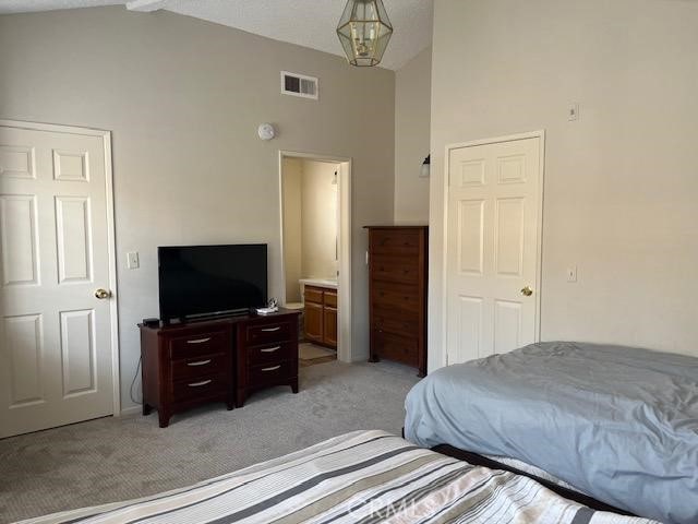 bedroom with ensuite bathroom, light carpet, high vaulted ceiling, and a chandelier