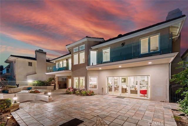 back house at dusk with french doors, a patio area, and a balcony