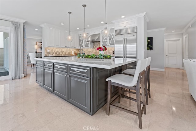 kitchen featuring built in fridge, hanging light fixtures, a center island with sink, and white cabinets