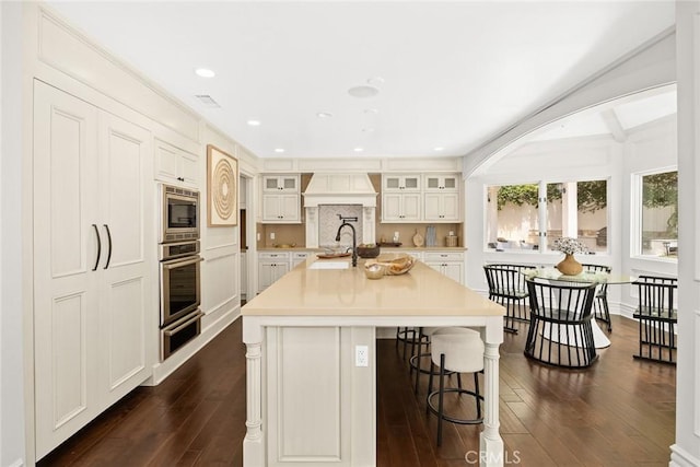 kitchen with sink, stainless steel appliances, a kitchen island with sink, and dark hardwood / wood-style floors